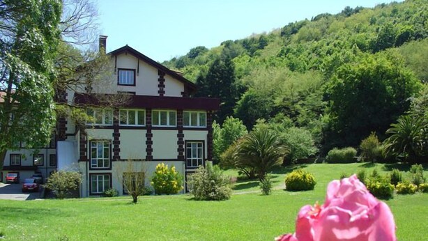 A large, two-story building with a symmetrical facade, surrounded by a well-maintained garden and a hillside. - Balneario Casa Pallotti (Valle de Carranza)
