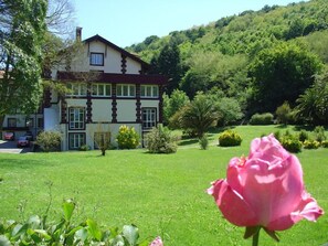 A large, two-story building with a symmetrical facade, surrounded by a well-maintained garden and a hillside. - Balneario Casa Pallotti (Valle de Carranza)
