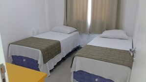 Una habitación con dos camas individuales, cada una con colchón blanco y manta marrón. A la izquierda, hay una mesa amarilla.