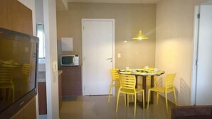 Una cocina compacta con microondas, una zona de comedor con mesa redonda y sillas amarillas, y una puerta blanca al fondo.