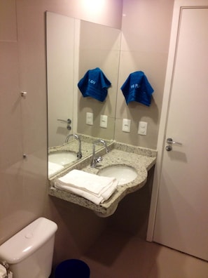 A bathroom with a granite sink, two faucets, and a mirror above it. There are towels stacked on the sink and a blue bucket on the floor. - Temporada Vg Fun Fortaleza (Fortaleza)