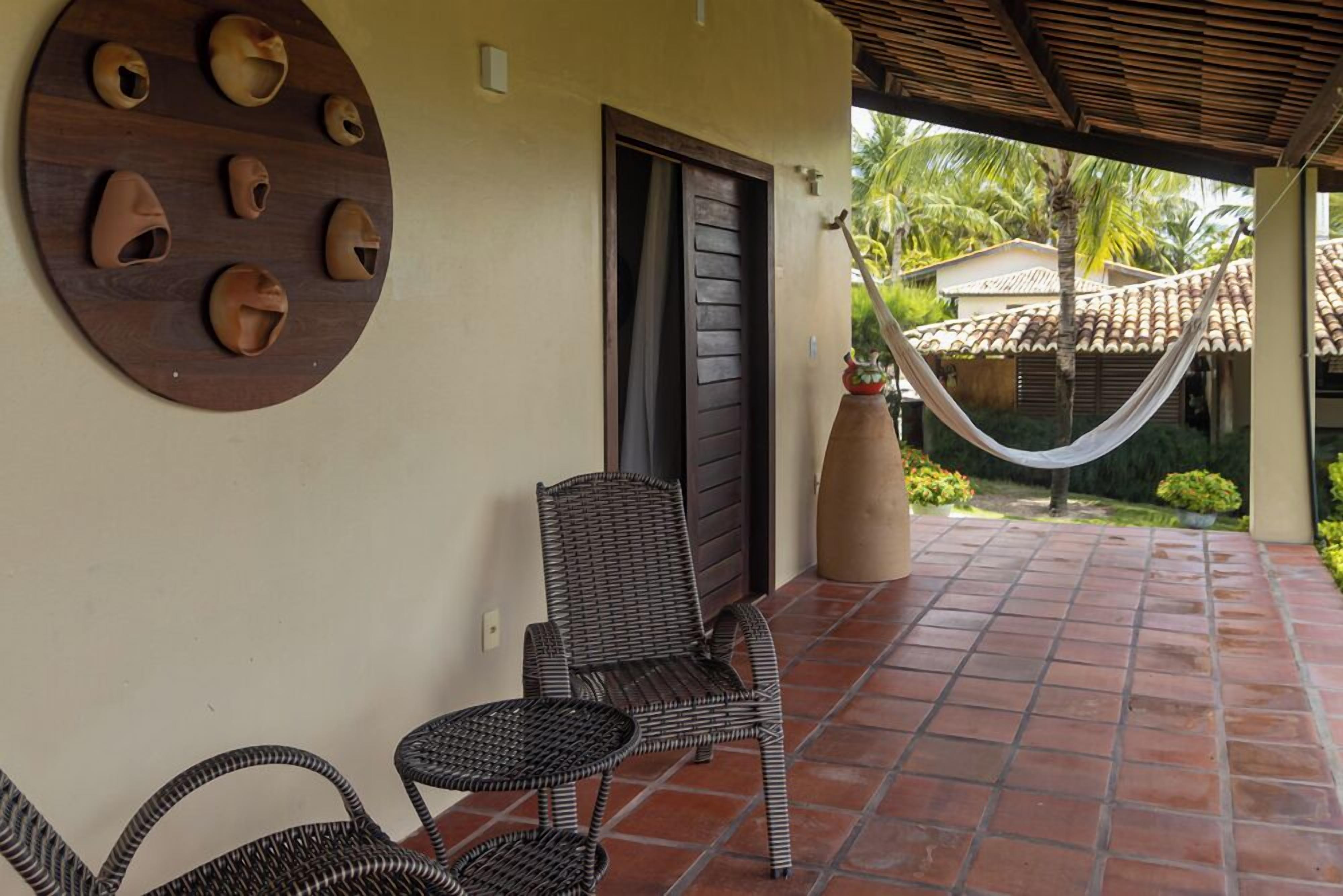 A covered patio with wicker furniture, a decorative wall, and a view of a garden with a hammock.