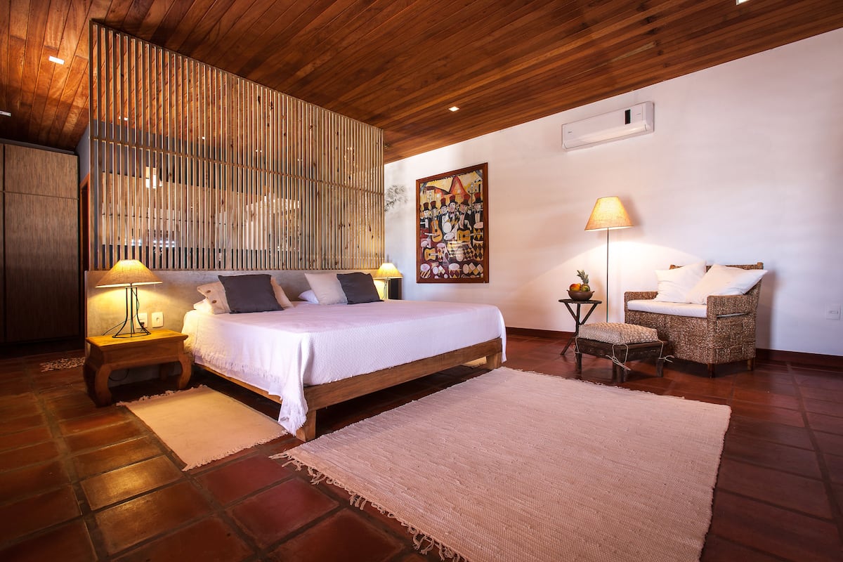 Un dormitorio con cama, mesitas de noche, una silla, alfombra y techo de madera.