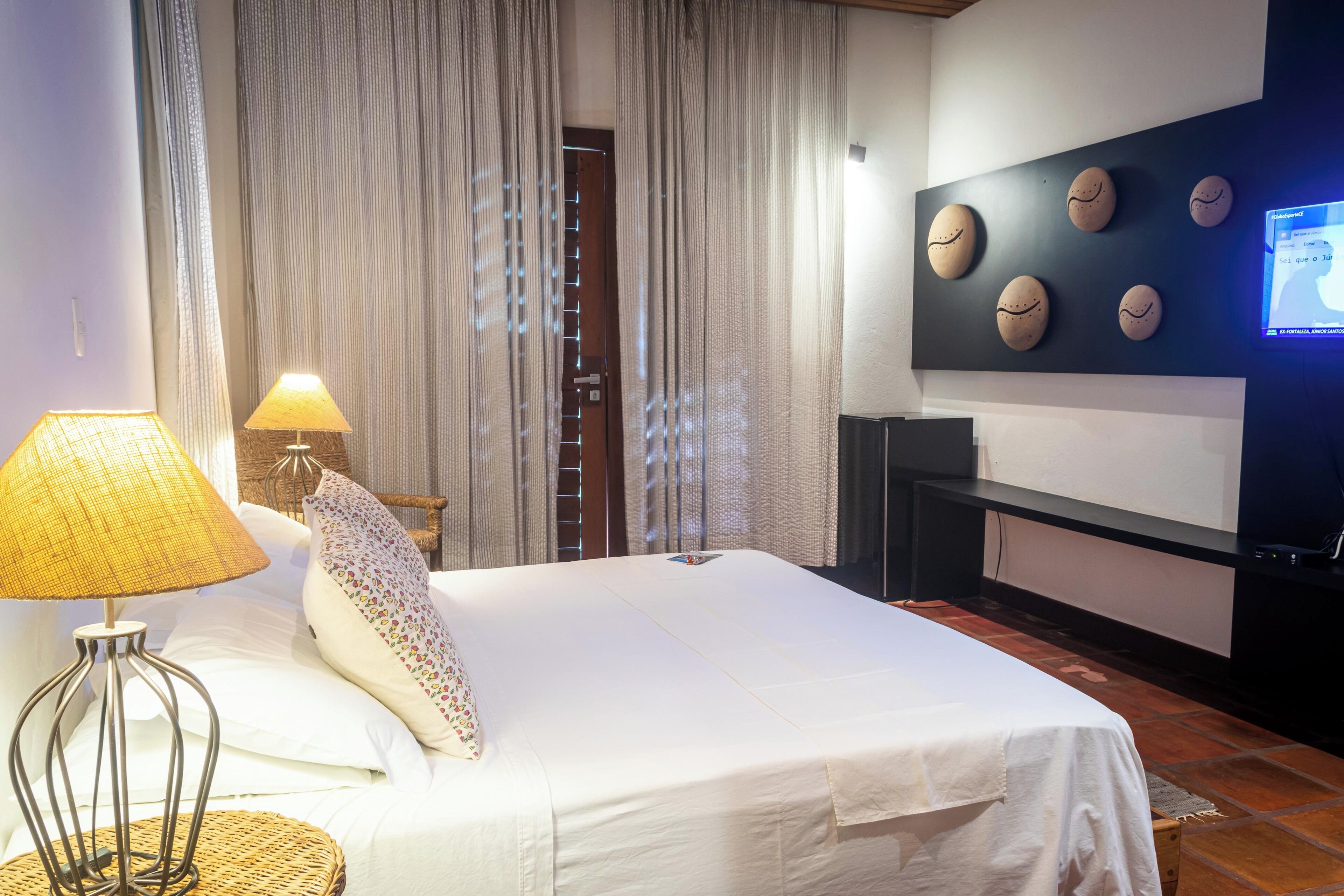 Una habitació d'hotel amb un llit, una làmpada, un televisor i una paret decorada.