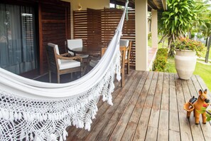 A hammock on a wooden deck, a wooden table with chairs, and a large planter with flowers.