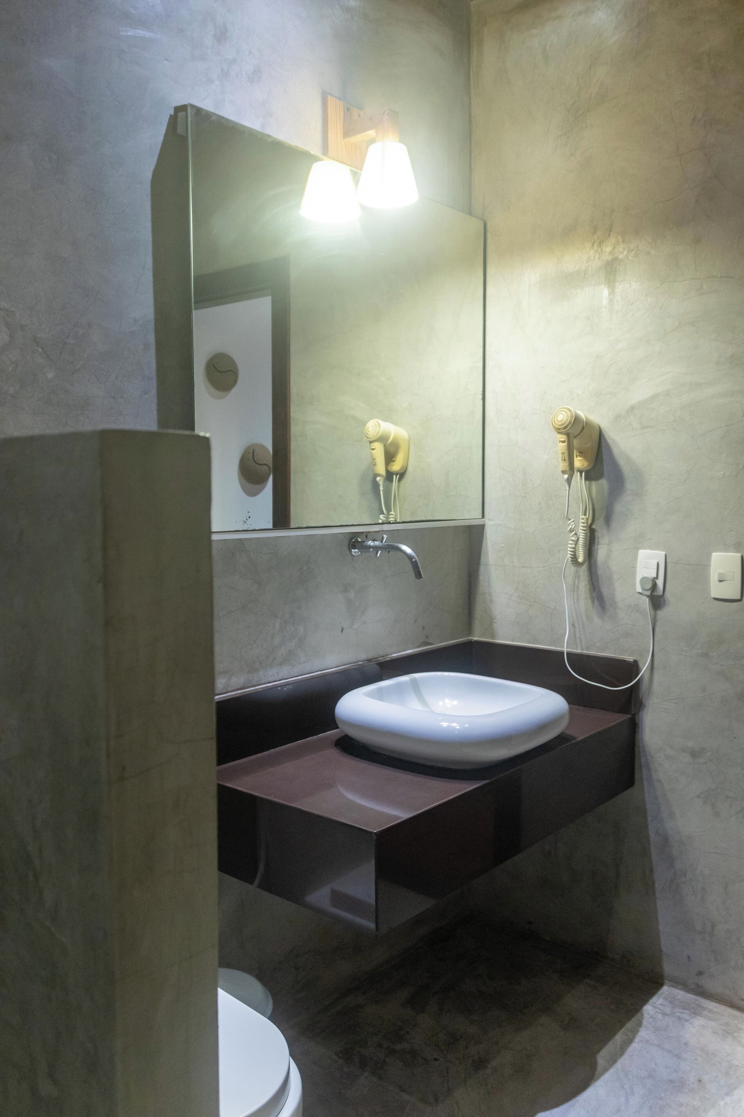 A bathroom with a white sink, a mirror, a hairdryer, and a toilet.