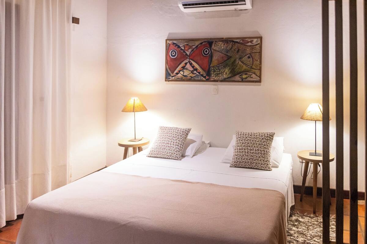 Una cama bien hecha con un edredón estampado, dos almohadas y una obra de arte colgada en la pared.