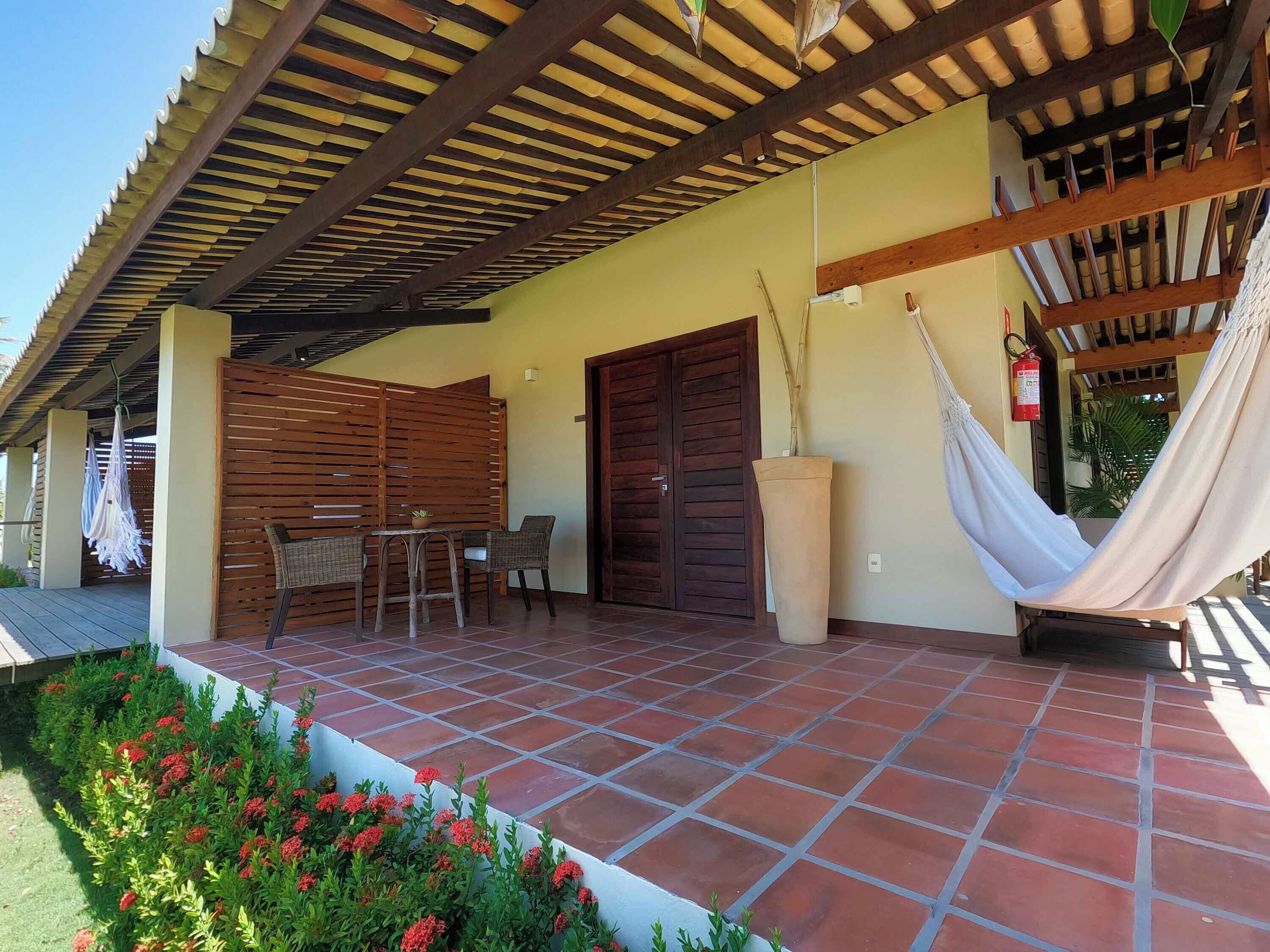 A covered patio area with a tiled floor, a wooden table with chairs, a hammock, and a large planter.