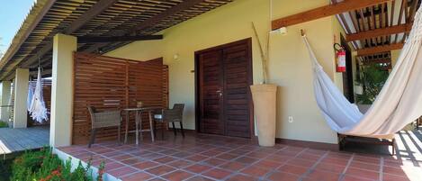 A covered patio area with a tiled floor, a wooden table with chairs, a hammock, and a large planter.