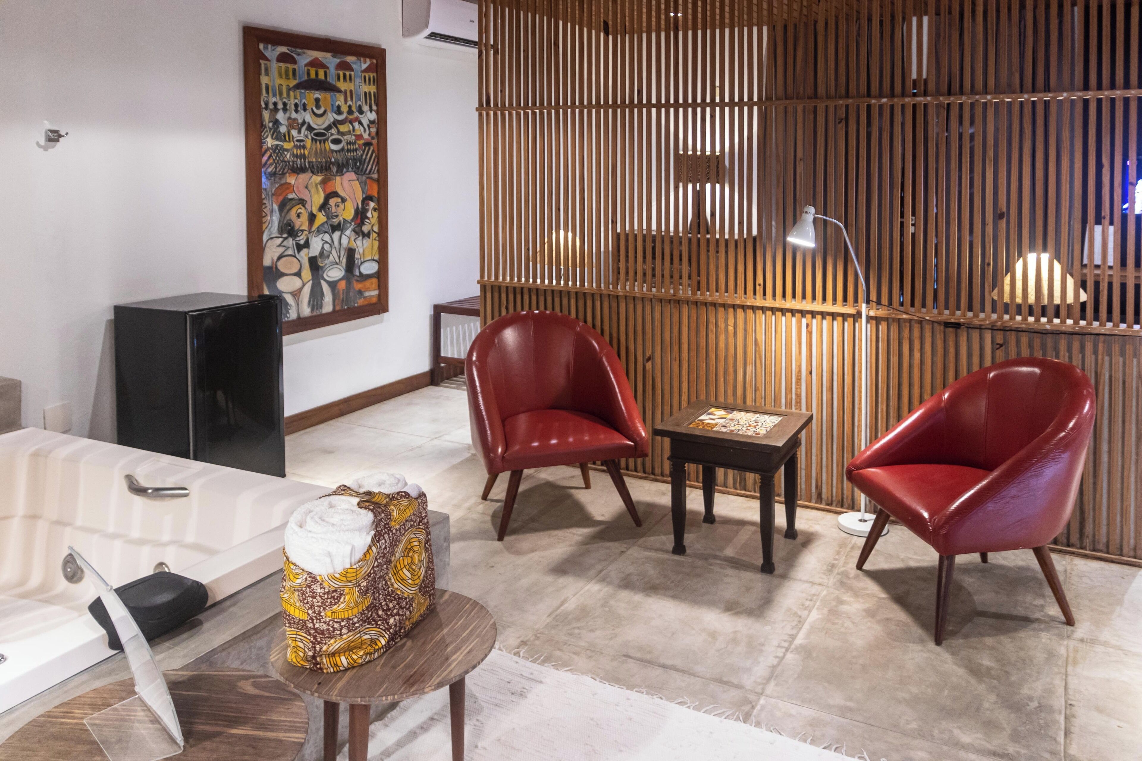 Un salon moderne avec une cloison en bois, deux fauteuils en cuir rouge, une petite table et un grand tableau accroché au mur.