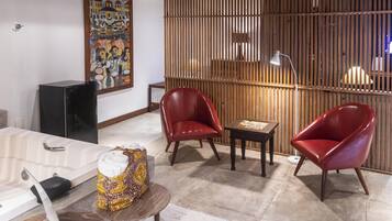Un salon moderne avec une cloison en bois, deux fauteuils en cuir rouge, une petite table et un grand tableau accroché au mur.