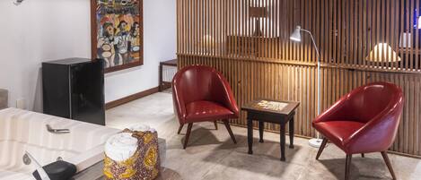Una sala de estar moderna con un separador de madera, dos sillones de cuero rojo, una mesita y un cuadro grande en la pared.