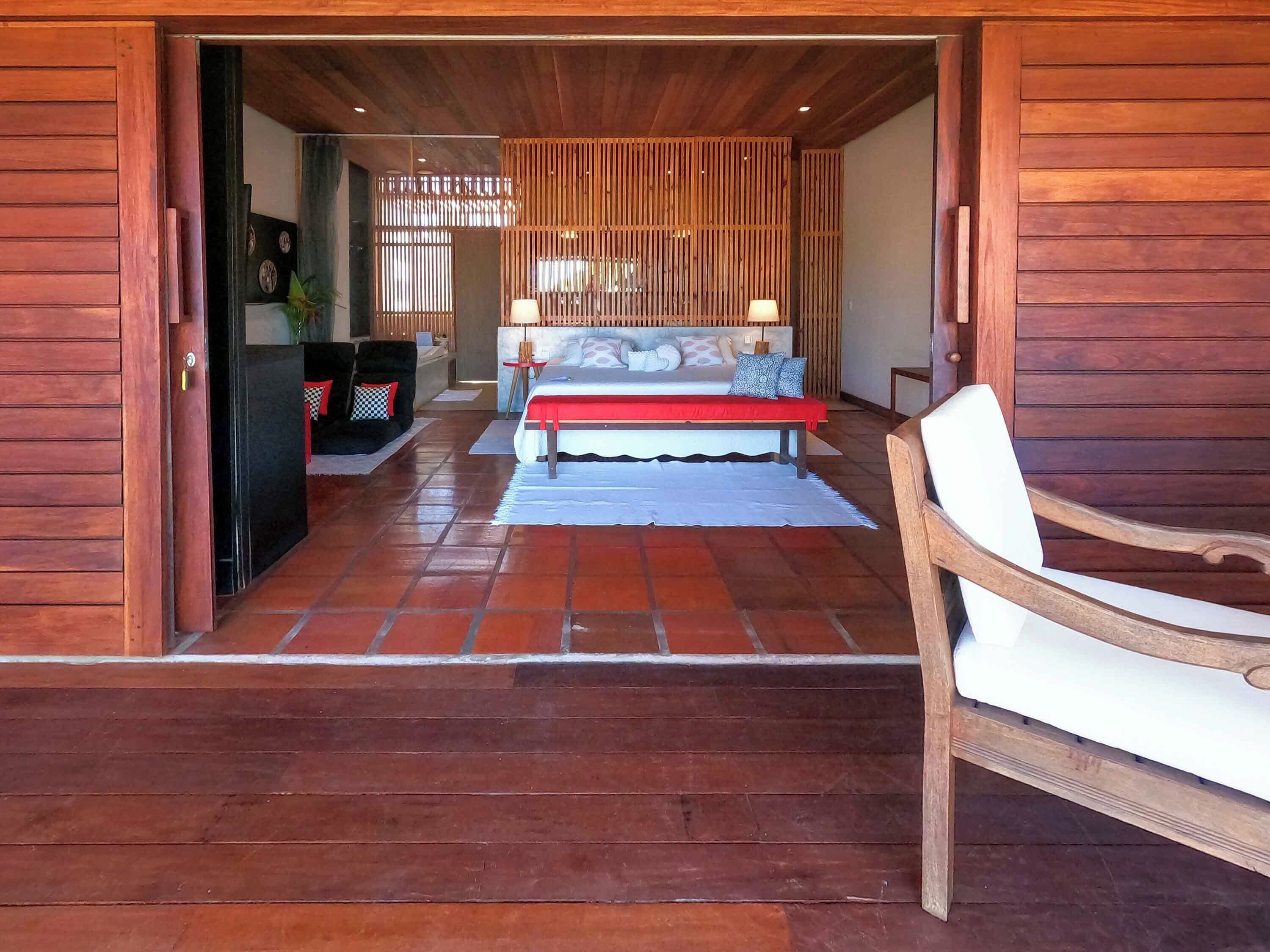 A wooden interior with a bed, a bench, and a door leading to another room.