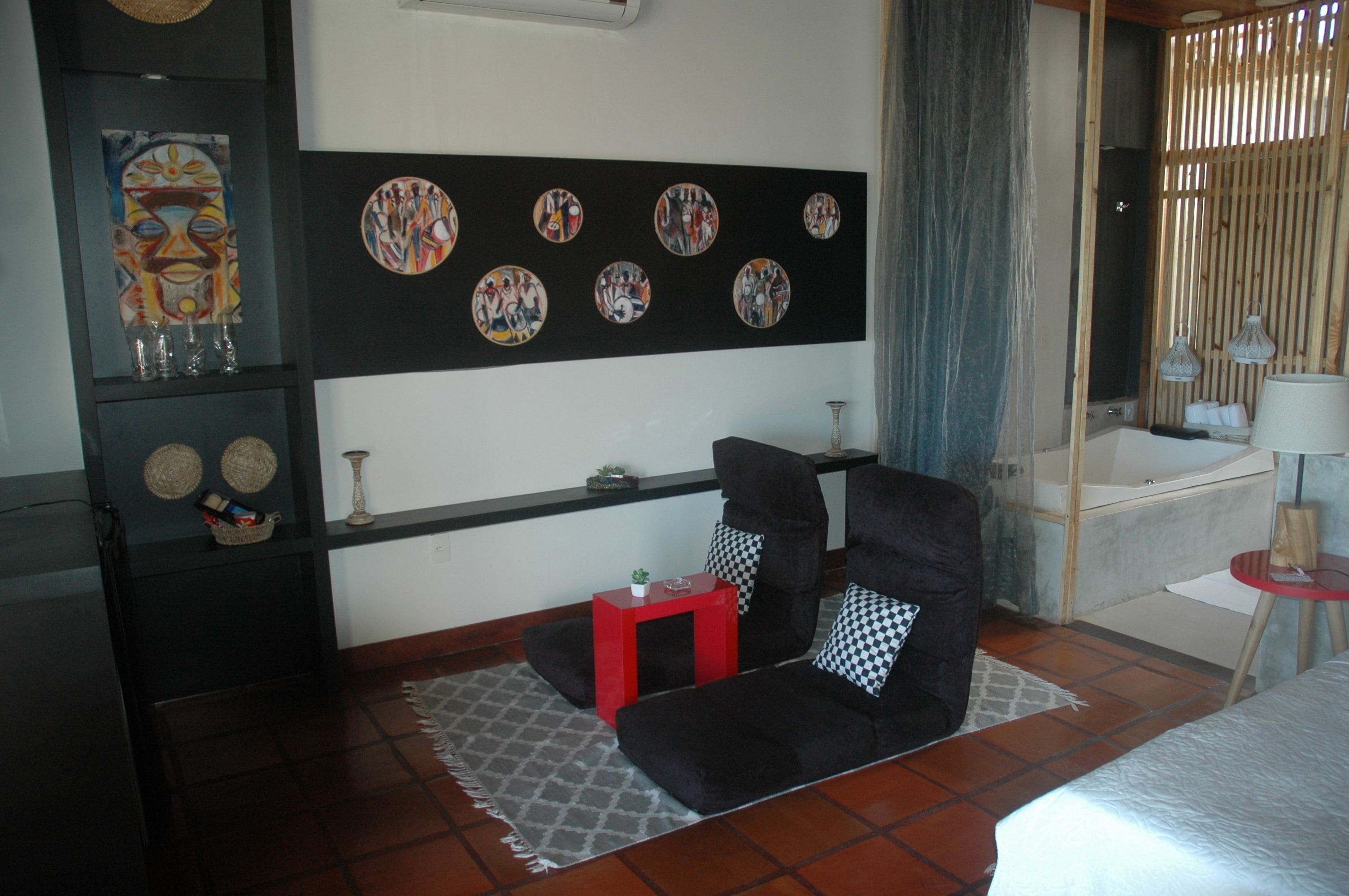 Una habitación con un sofá negro, una mesita auxiliar roja, una alfombra estampada y una pared con una obra de arte circular.