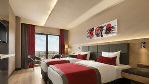 A hotel room with two beds, a desk, and a chair. There is a large window with a view of the city. - Ramada Encore by Wyndham Gebze (Gebze)