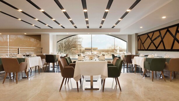A spacious dining area with multiple tables and chairs, a modern ceiling design with linear lighting, and large windows offering a view of the outside. - Ramada Encore by Wyndham Gebze (Gebze)