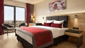 A modern hotel room with a large bed, a balcony with a view, a desk, and a chair. - Ramada Encore by Wyndham Gebze (Gebze)