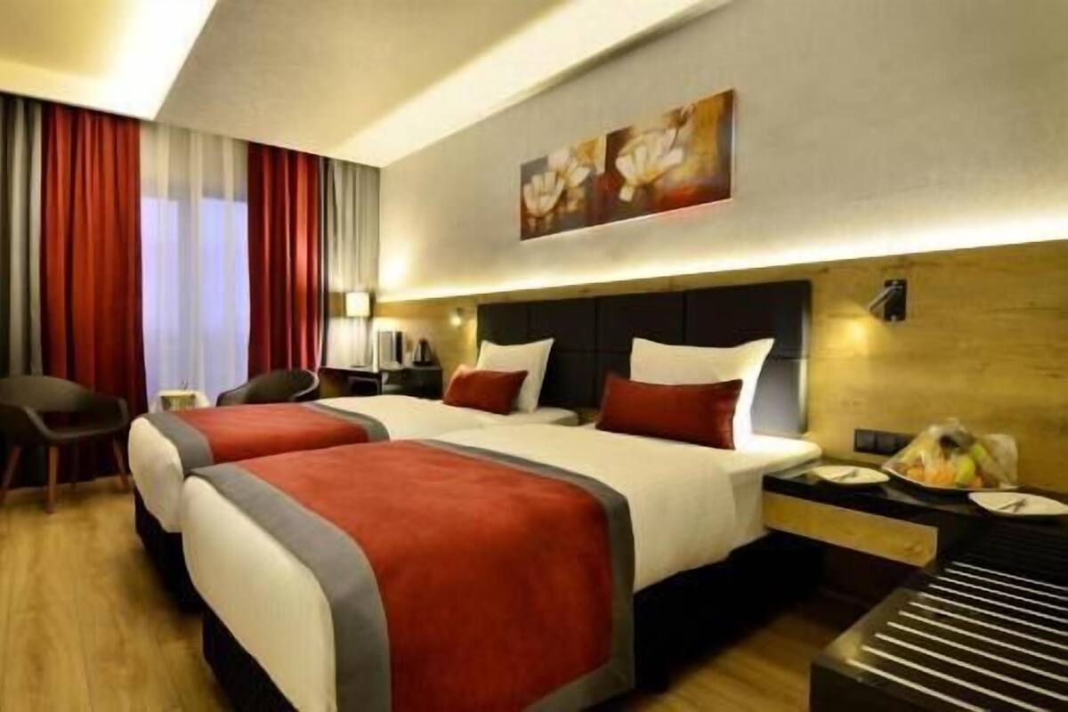 A hotel room with two beds, a desk, a chair, and a painting on the wall.