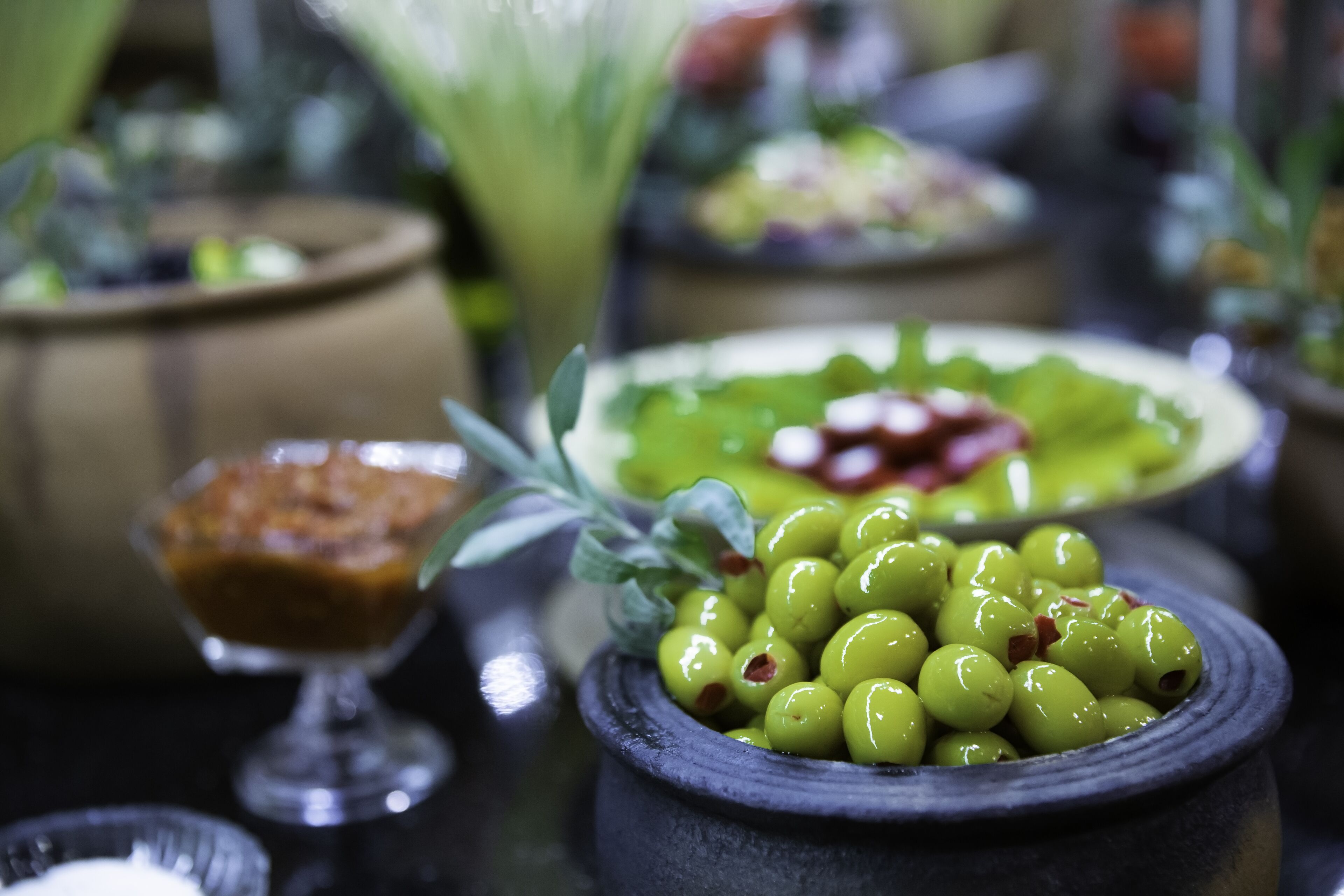 A table with various dishes, including olives, a green salad, and a dessert in a glass bowl.