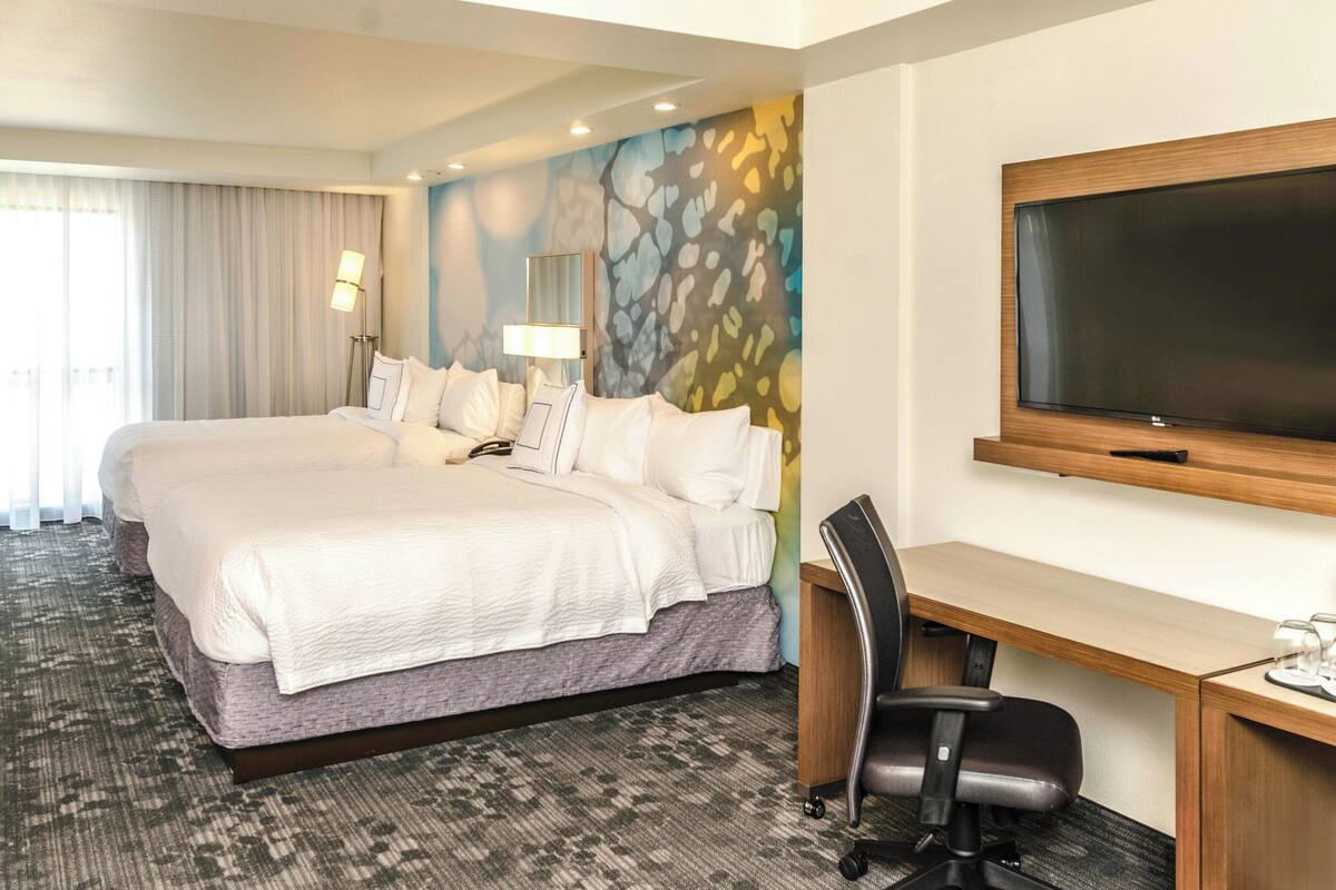 A hotel room with a large bed, a desk, a chair, a flat-screen TV, and a wall with a colorful abstract design.