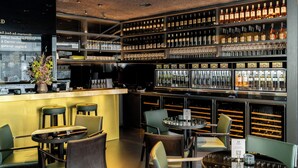 Un espace bar doté de plusieurs étagères remplies de bouteilles et de verres, de tabourets de bar et de tables.