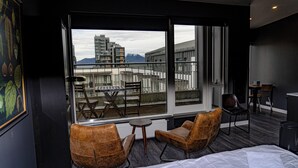 Une chambre d’hôtel avec une grande fenêtre, deux fauteuils en cuir, une petite table ronde et un lit.