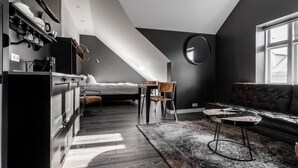 Une chambre de style loft moderne avec un plafond en pente, un grand lit, un coin repas avec une table et des chaises, et un canapé en cuir noir.