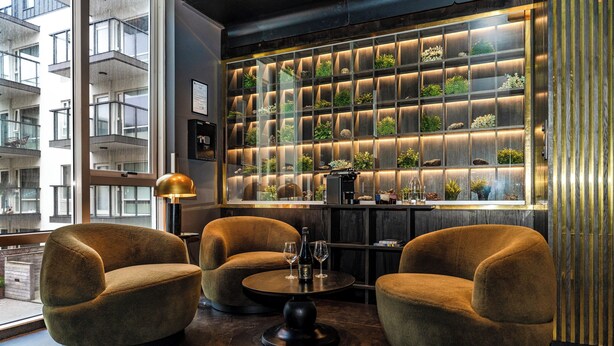 Un espace bar moderne avec deux tables rondes, deux fauteuils confortables et un mur décoré de jardinières éclairées.