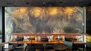 Un restaurant orné d’une grande fresque représentant des feuilles tropicales, doté de sièges confortables et de tables rondes.