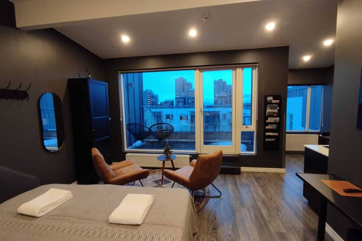 Ein modernes Hotelzimmer mit großem Fenster, einem Bett, einem Schreibtisch und zwei Stühlen.