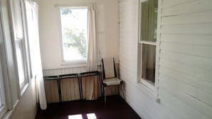 A room with white walls, a dark wooden floor, a window with curtains, and a chair.