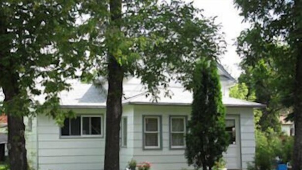 A single-story house with a gabled roof, surrounded by mature trees and a well-maintained lawn.