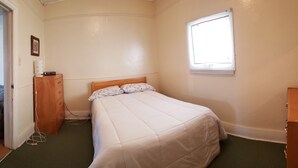 Ein Schlafzimmer mit Bett, Kommode, Fenster und Tür.
