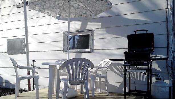 Eine Terrasse mit Gartenmöbeln, einem Grill und einem Fernsehbildschirm.