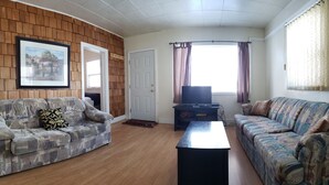 Ein Wohnzimmer mit zwei gemusterten Sofas, einem Couchtisch, einem Fernseher auf einem Schrank und einem gerahmten Bild an der Wand.