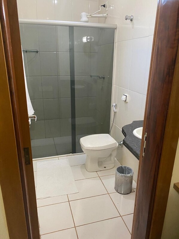 A bathroom with a glass-enclosed shower, a toilet, a sink, and a trash bin.