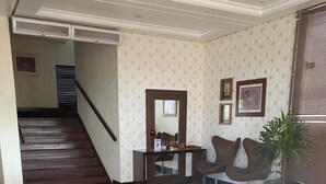 Un vestíbulo con una escalera, un mostrador de recepción, dos sillas, un sofá y una planta en maceta.