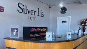 Mostrador de recepción de hotel con detalles de madera, un reloj y un cartel que indica el nombre del hotel 'Silver Las Hotel'.