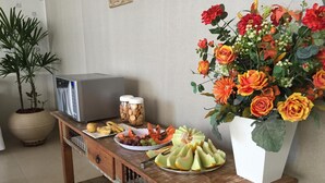 Una consola de madera con un microondas, frascos de galletas, un plato de fruta y un florero.