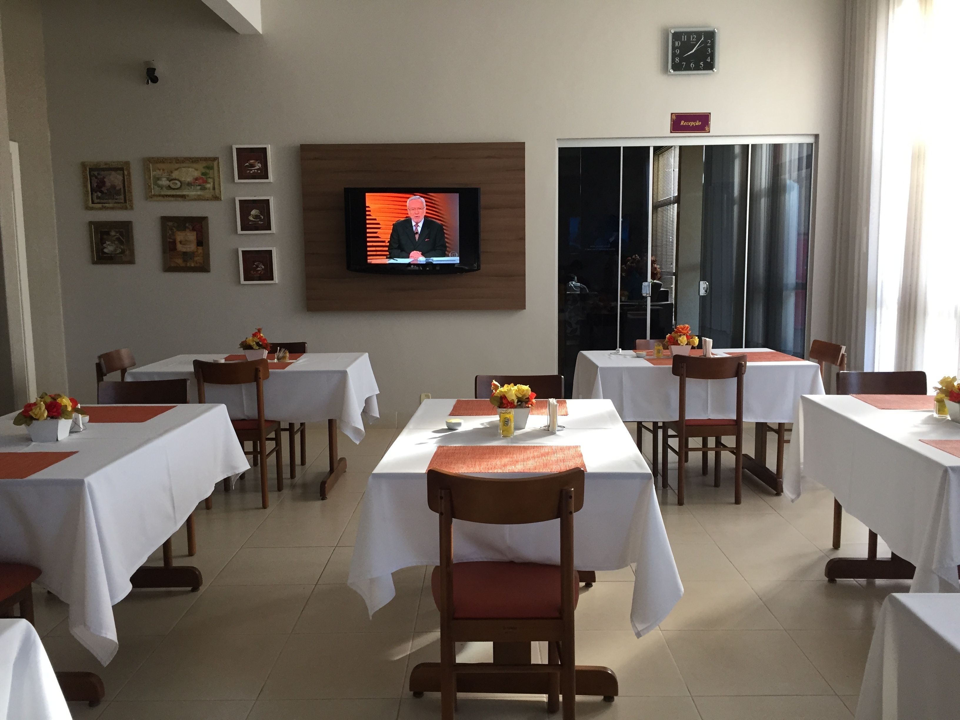 A dining area with tables set for service, a television mounted on the wall, and framed pictures on the wall.