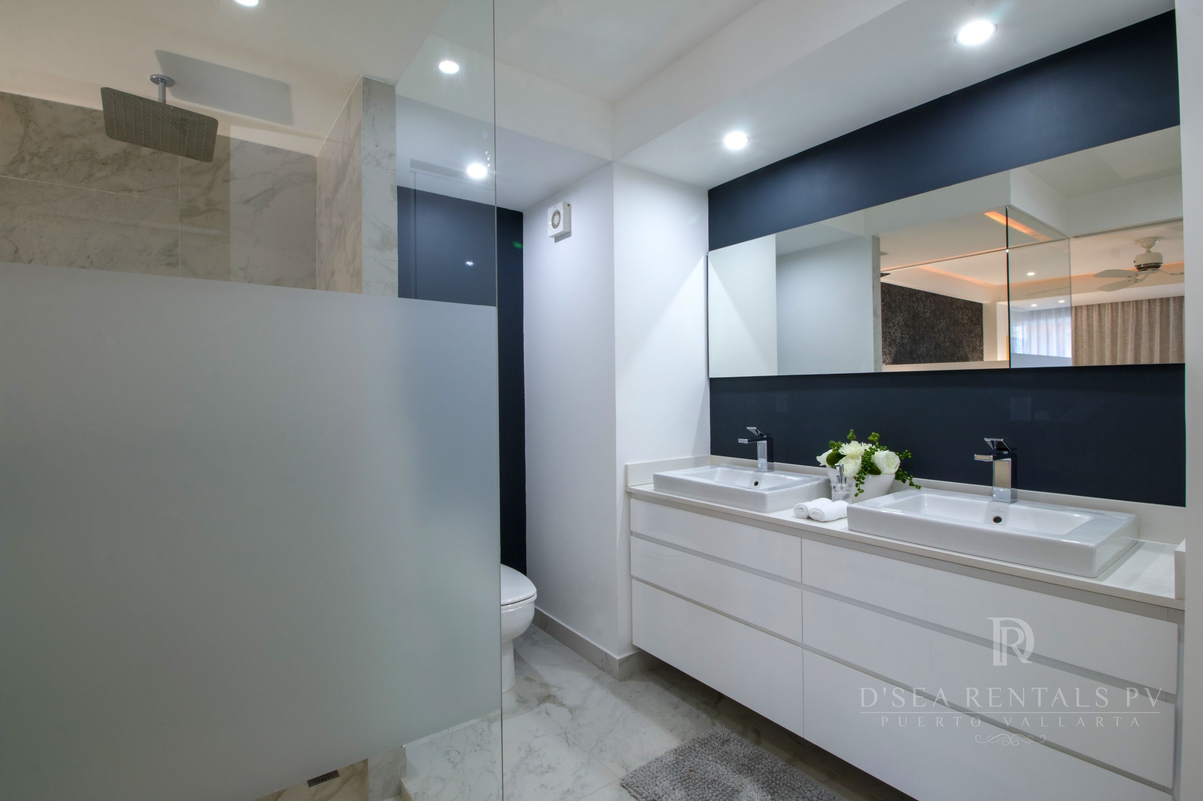 A modern bathroom with a large mirror, two sinks, and a shower.