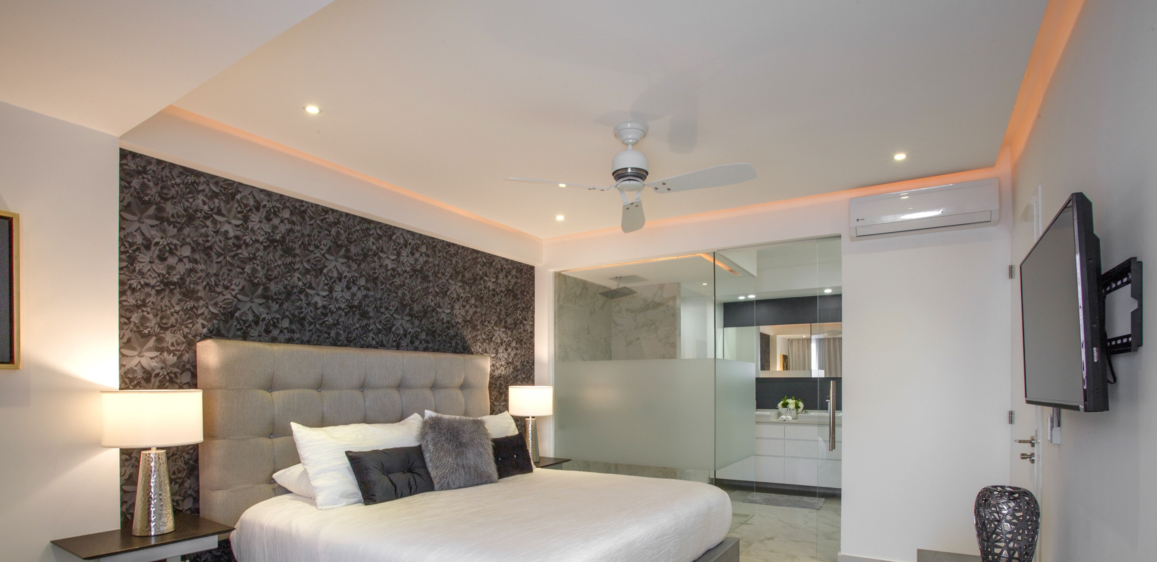 Una camera d'albergo moderna con un letto grande, una ventola a soffitto, una televisione a schermo piatto e un box doccia in vetro.