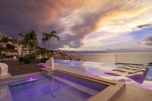 A rooftop infinity pool with a view of the sea and mountains, palm trees, and a wooden deck. - D Terrace Luxury Residences (Puerto Vallarta)