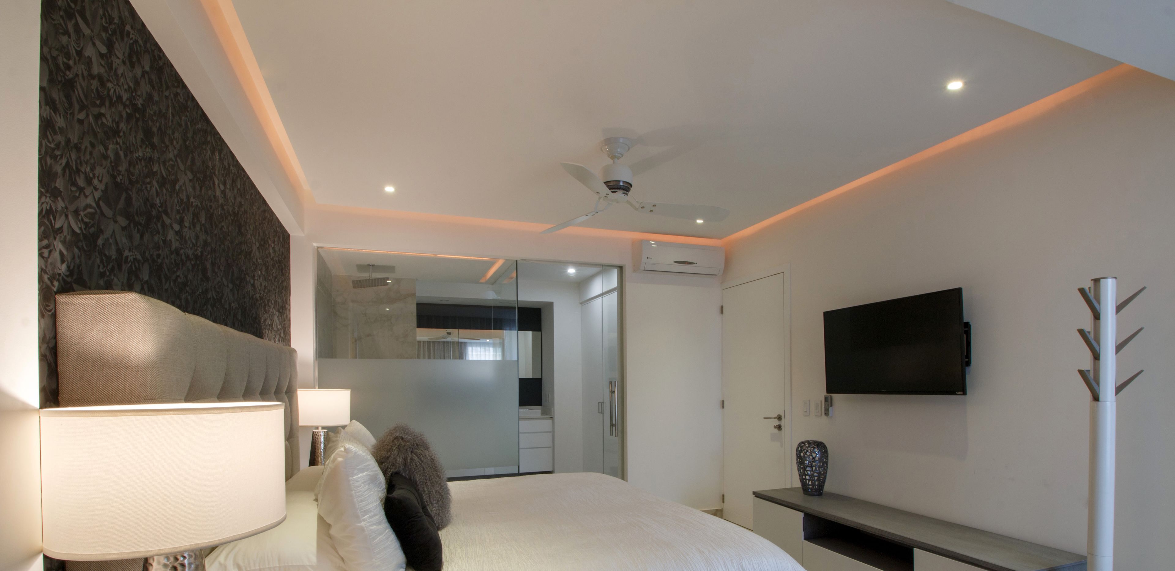Un dormitorio moderno con cama, televisor, ventilador de techo y un espejo grande.