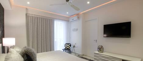 Una habitación de hotel moderna con una cama, un televisor montado en la pared, un ventilador de techo y una ventana con cortinas.