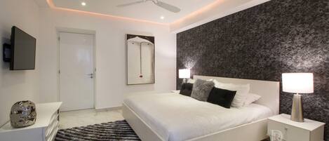 A modern bedroom with a large bed, bedside tables, a ceiling fan, and a decorative mirror.