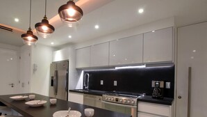 Una cocina moderna con electrodomésticos de acero inoxidable, una encimera negra e iluminación colgante.