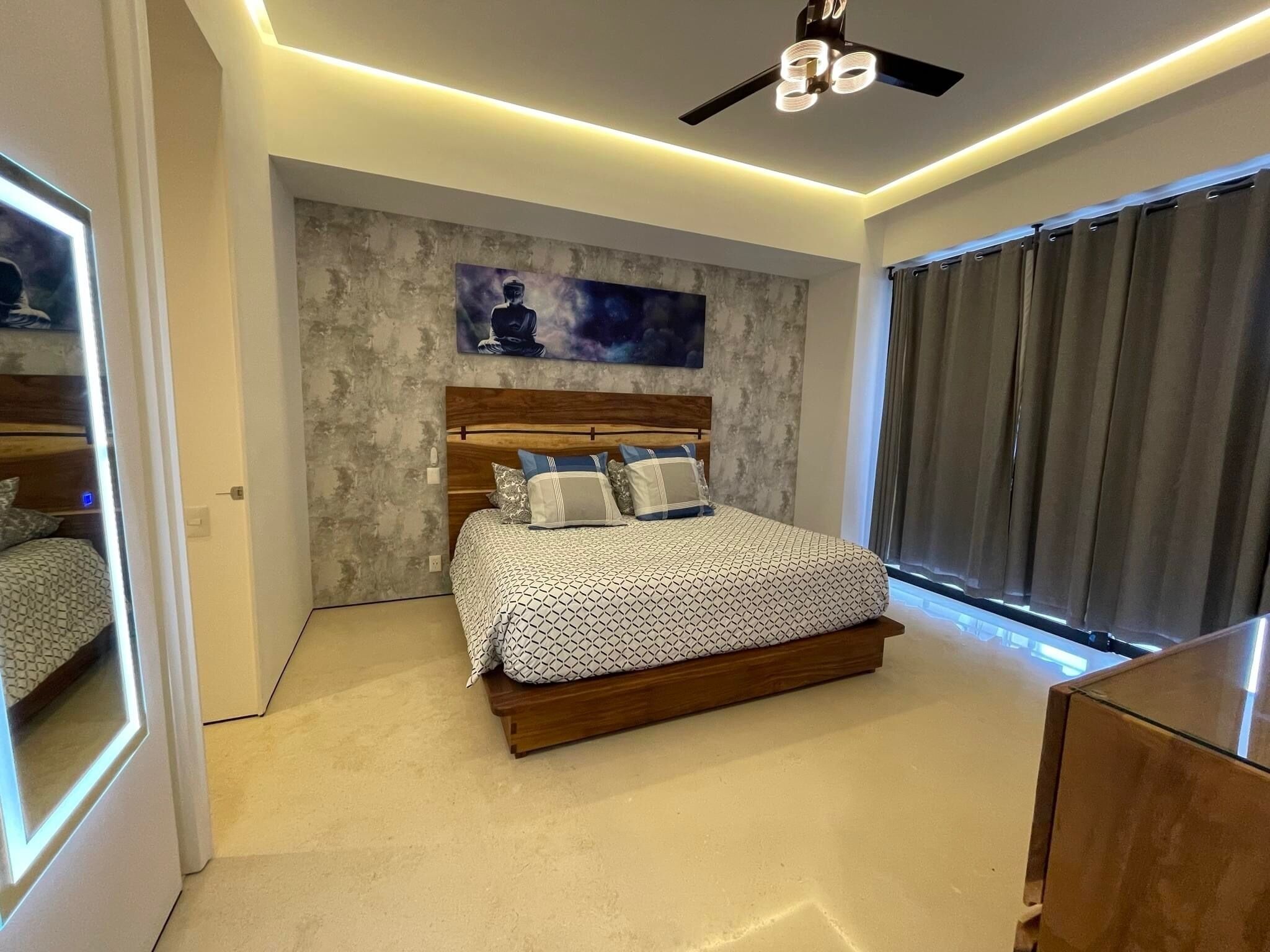 A modern bedroom with a large bed, a ceiling fan, and a painting on the wall.