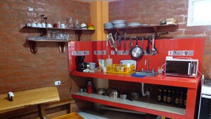 Cozinha com bancada vermelha, banco de madeira e diversos utensílios e eletrodomésticos.