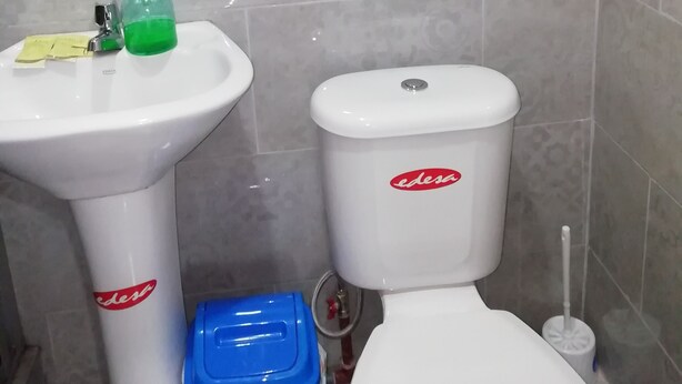 A bathroom with a white pedestal sink, a toilet, and a blue trash bin. - Hotel La Casa Amarilla City (Baños de Agua Santa)